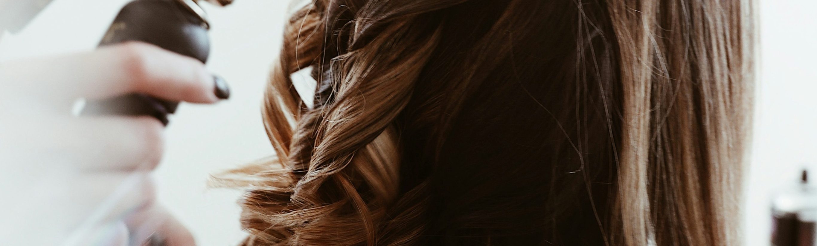 Eine Hand hält ein Haarglättergerät, während Haare in Locken geformt werden.